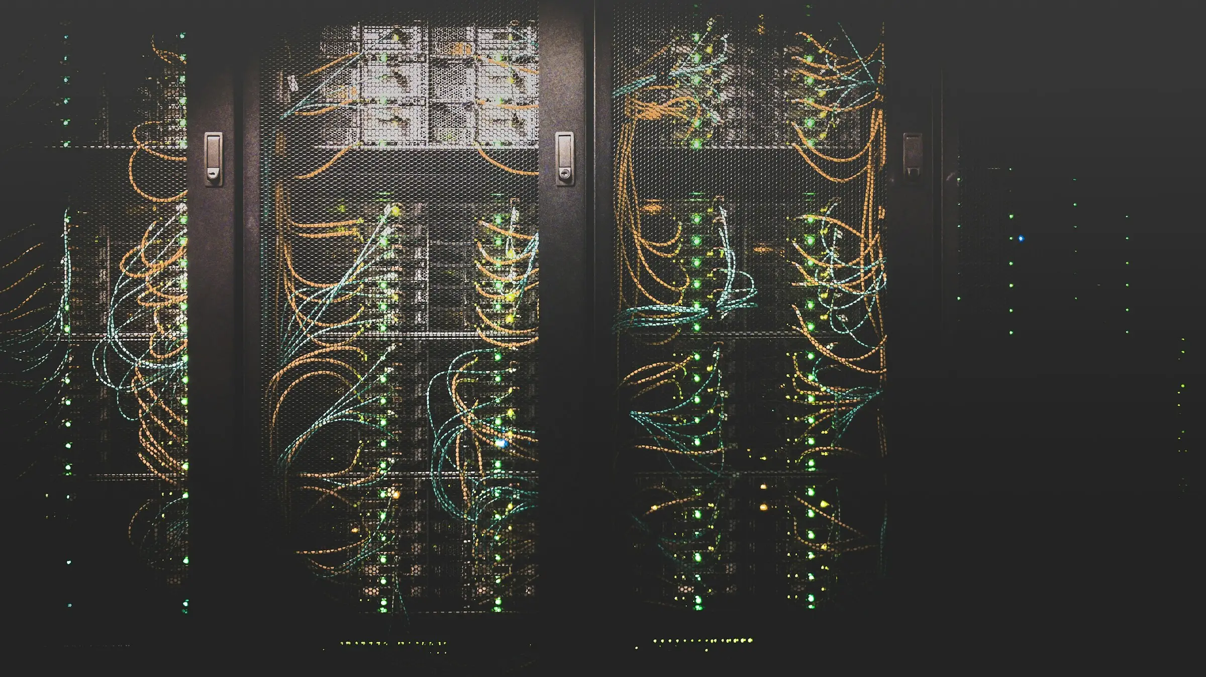 Network cabling running through a rack of servers in a dark equipment room.