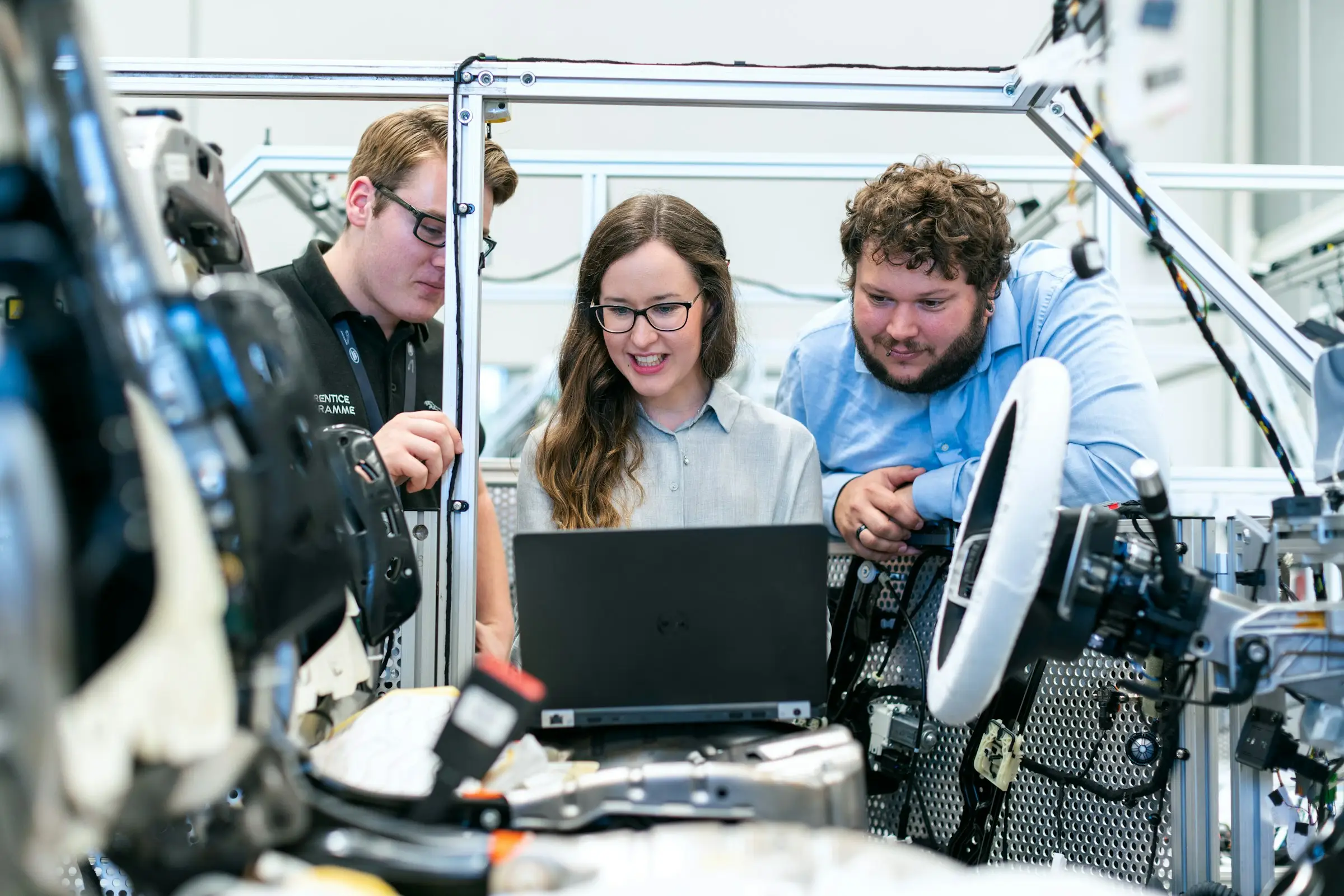 Three engineers reviewing a laptop together in an assembly workspace.
